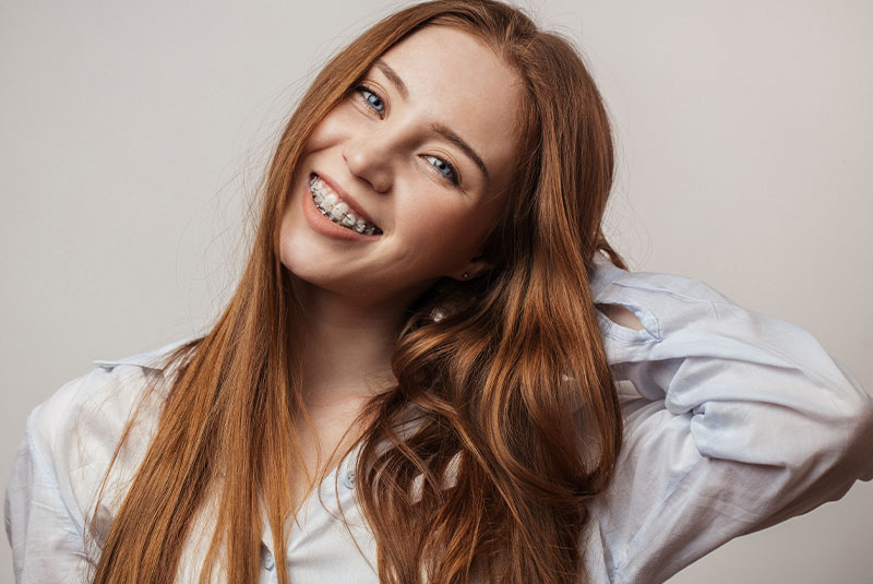 Happy young red-haired woman in braces smiling on white background looking at camera