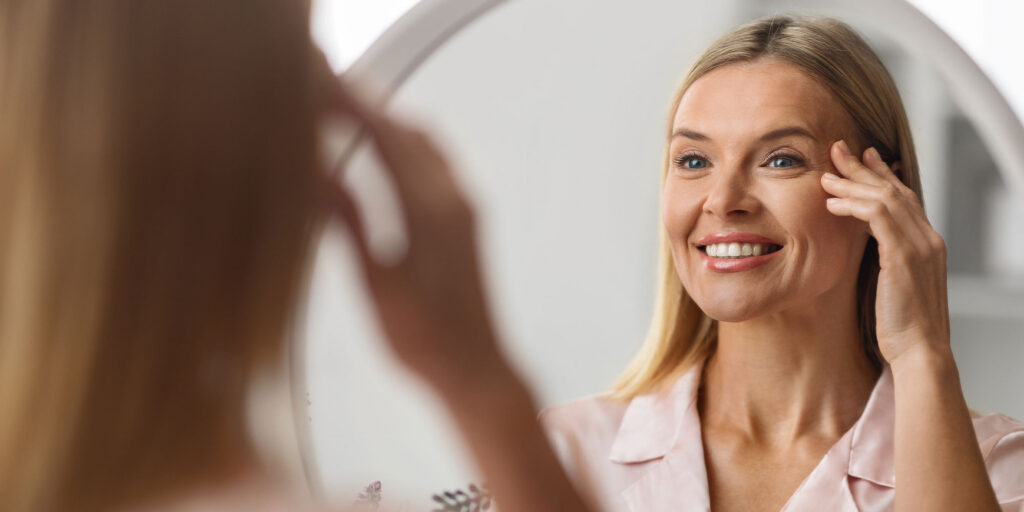 Cheerful mature woman looking at mirror at home smiling