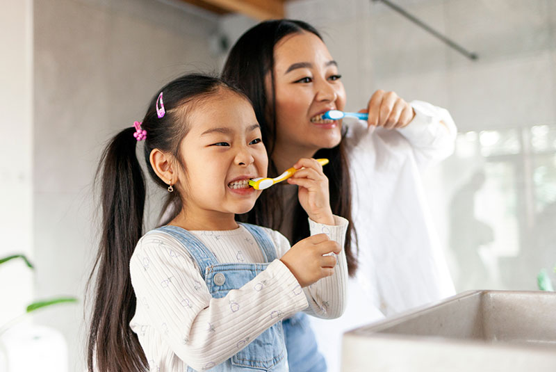 little girl with mom brushing teeth in bathroom